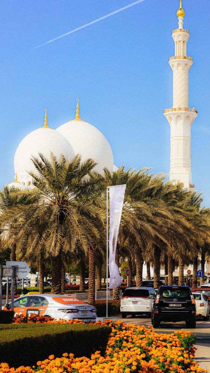 Stunning view of a mosque with palm trees and parked cars under a clear blue sky.