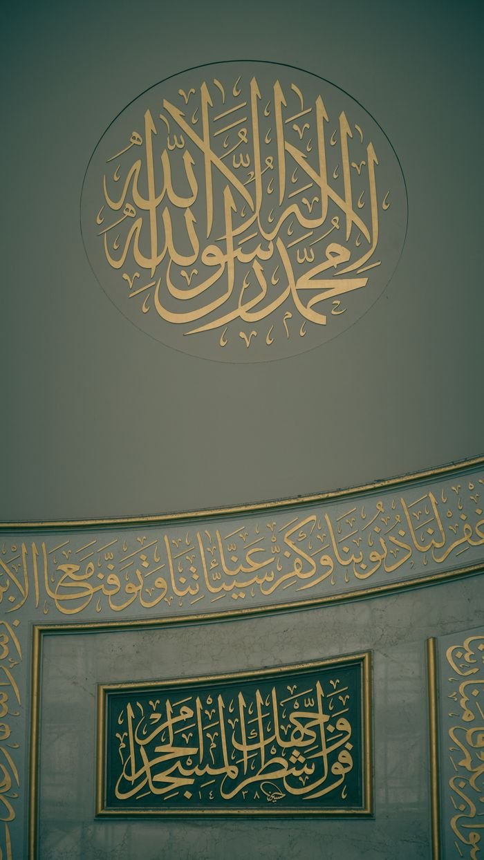 Intricate gold Islamic calligraphy on mosque wall interior, showcasing religious art.